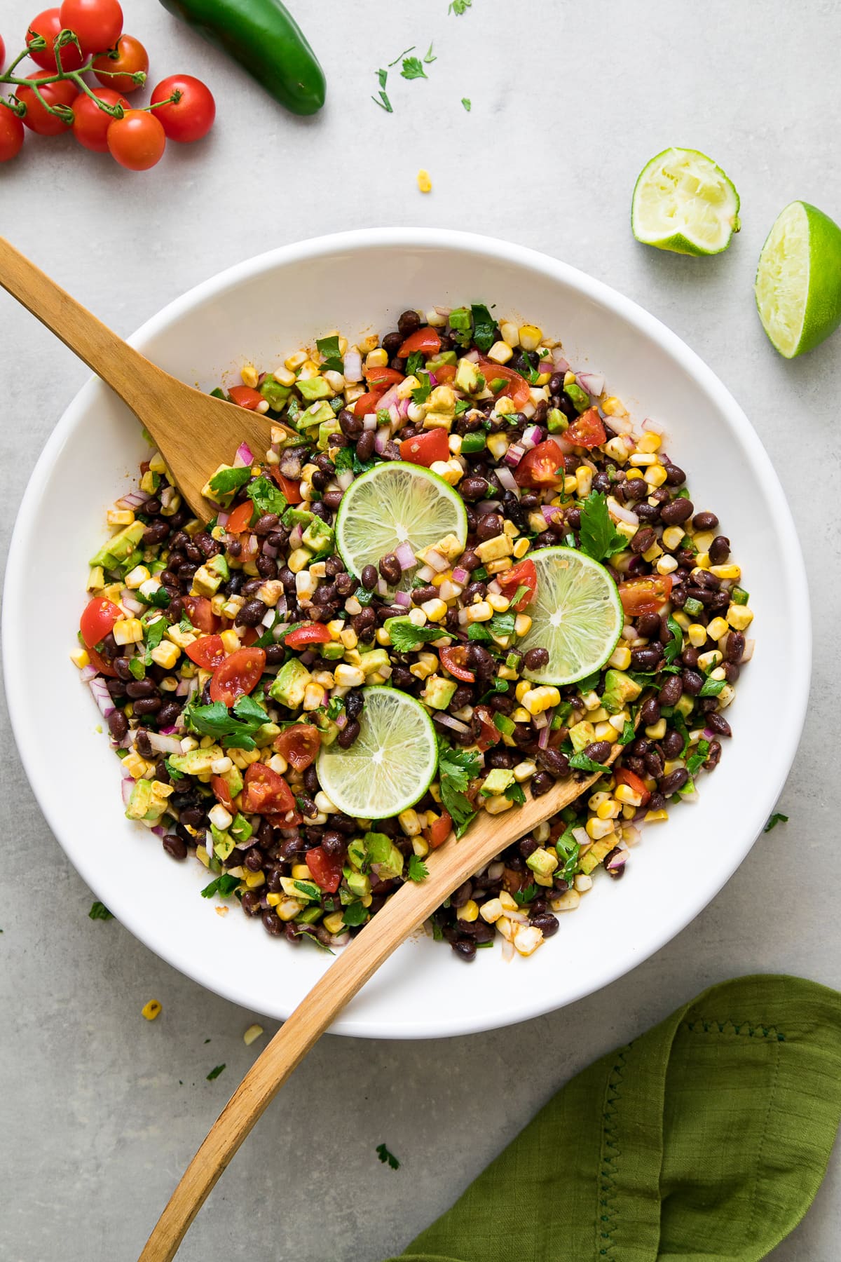 top down view of freshly mixed black bean corn salad in a large white bowl with wooden salad utensils.