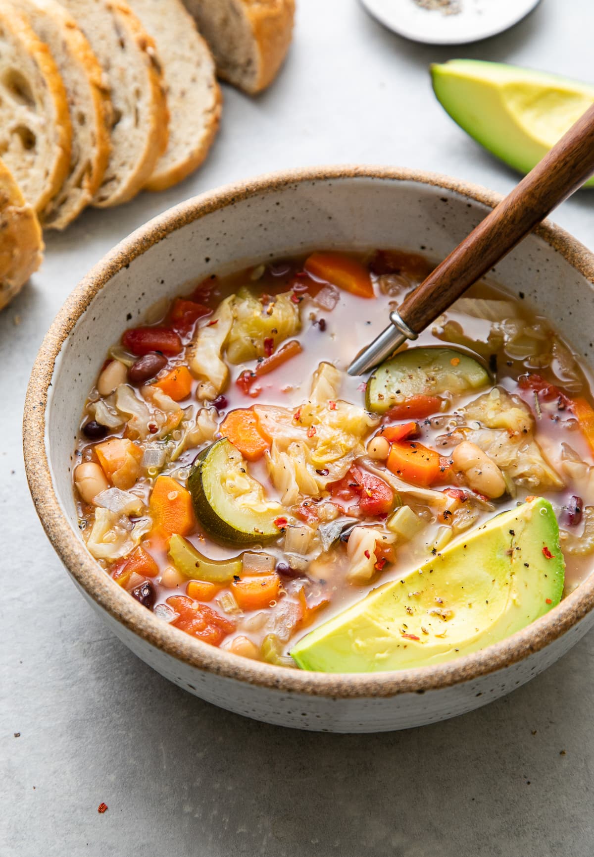 side angle view of bowl of vegetable quinoa soup with spoon and items surrounding.