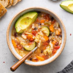 top down view of bowl of vegetable quinoa soup with spoon and items surrounding.