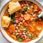top down view healthy black eyed pea soup in a bowl with cornbread.