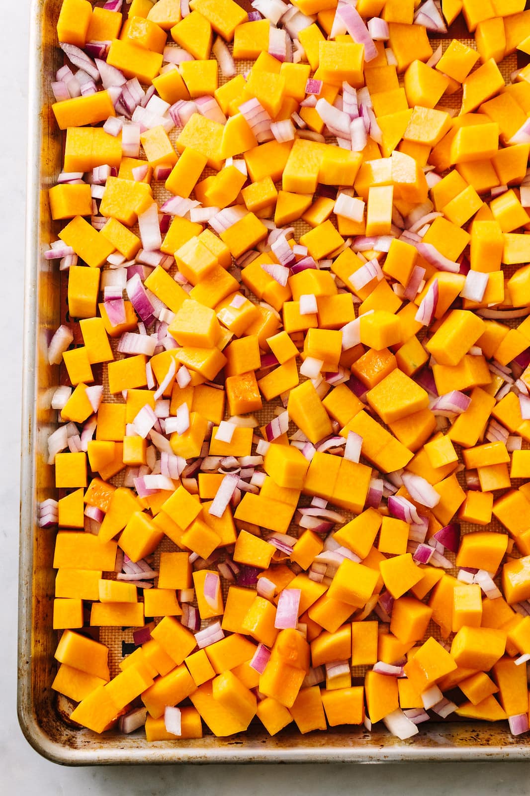 top down view of butternut squash and red onion on a rimmed baking sheet ready for the oven.