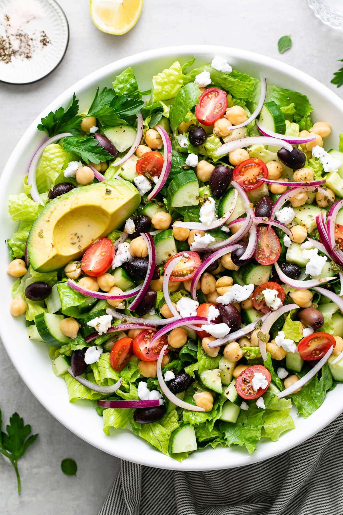 top down view of mediterranean chop salad in a white bowl with items surrounding.