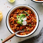 top down view of a serving of easy vegetable chili in a white bowl with black rim and wooden spoon.