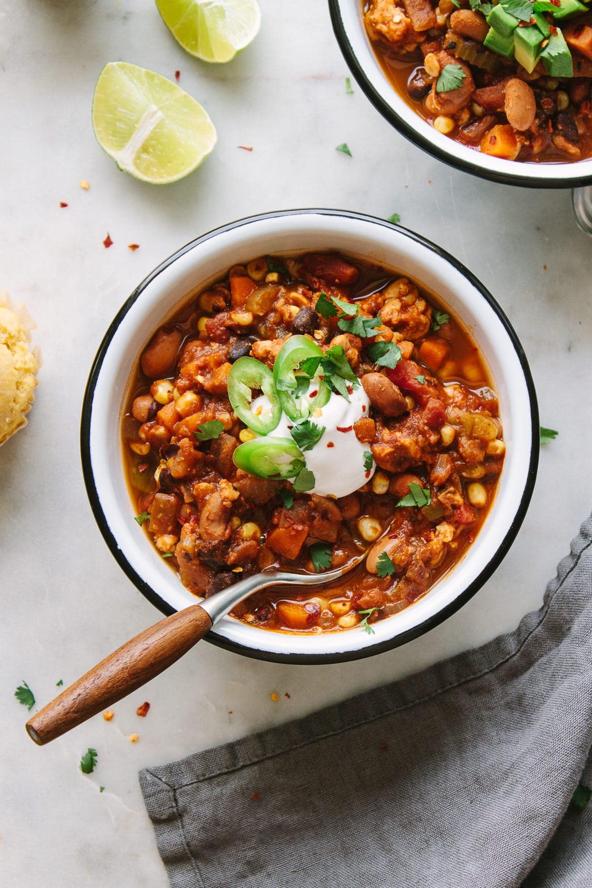 top down view of a serving of easy vegetable chili in a white bowl with black rim and wooden spoon.