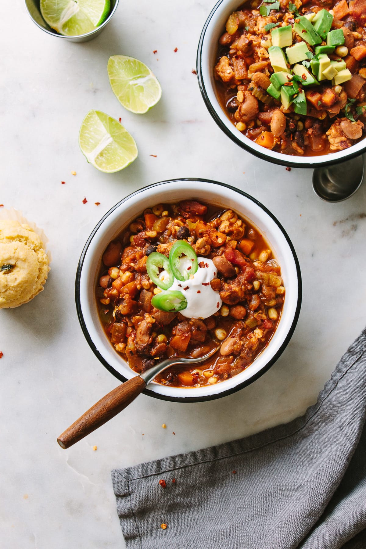 top down view of a serving of easy vegetable chili in a white bowl with black rim and spoon, with items surrounding.