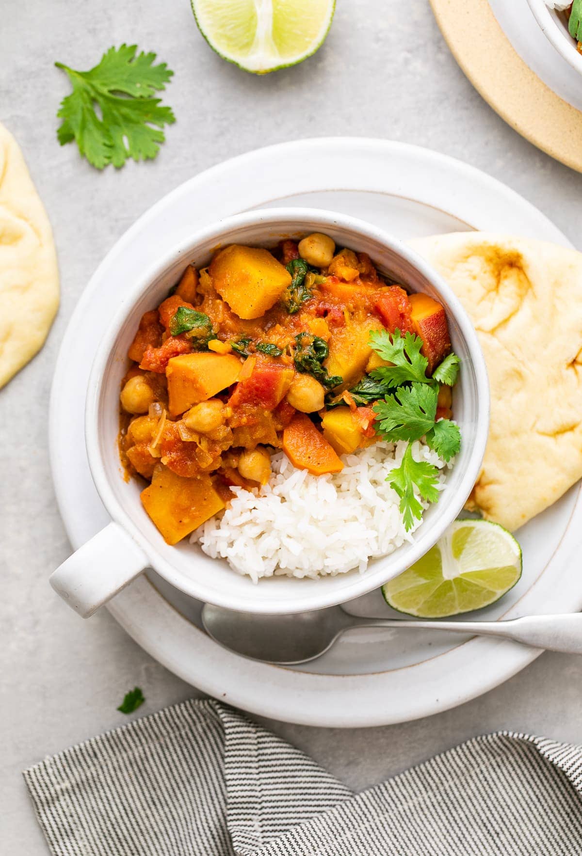 top down view of bowl with serving of moroccan pumpkin and chickpea stew with rice and items surrounding.