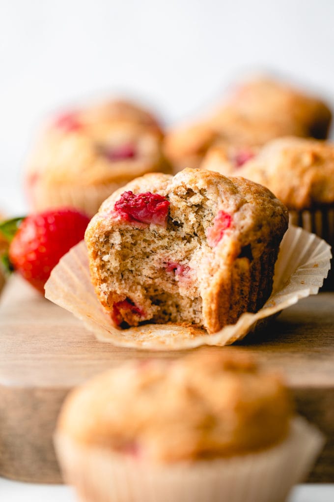 side angle view of strawberry banana muffin with bite eaten and items surrounding.