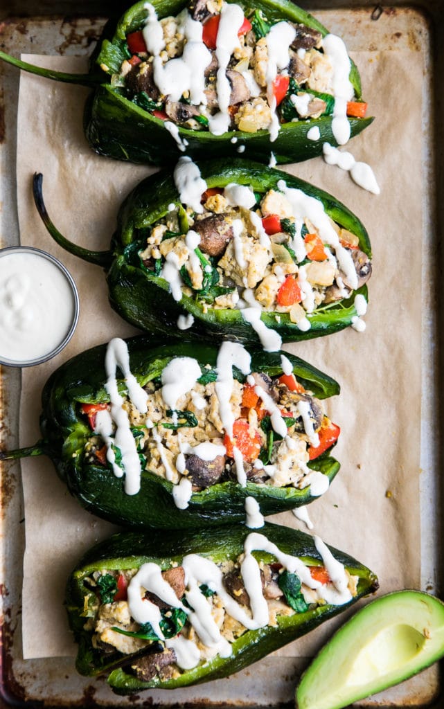 top down view of stuffed poblano peppers with tofu scramble and drizzled with cashew cream on a baking sheet.