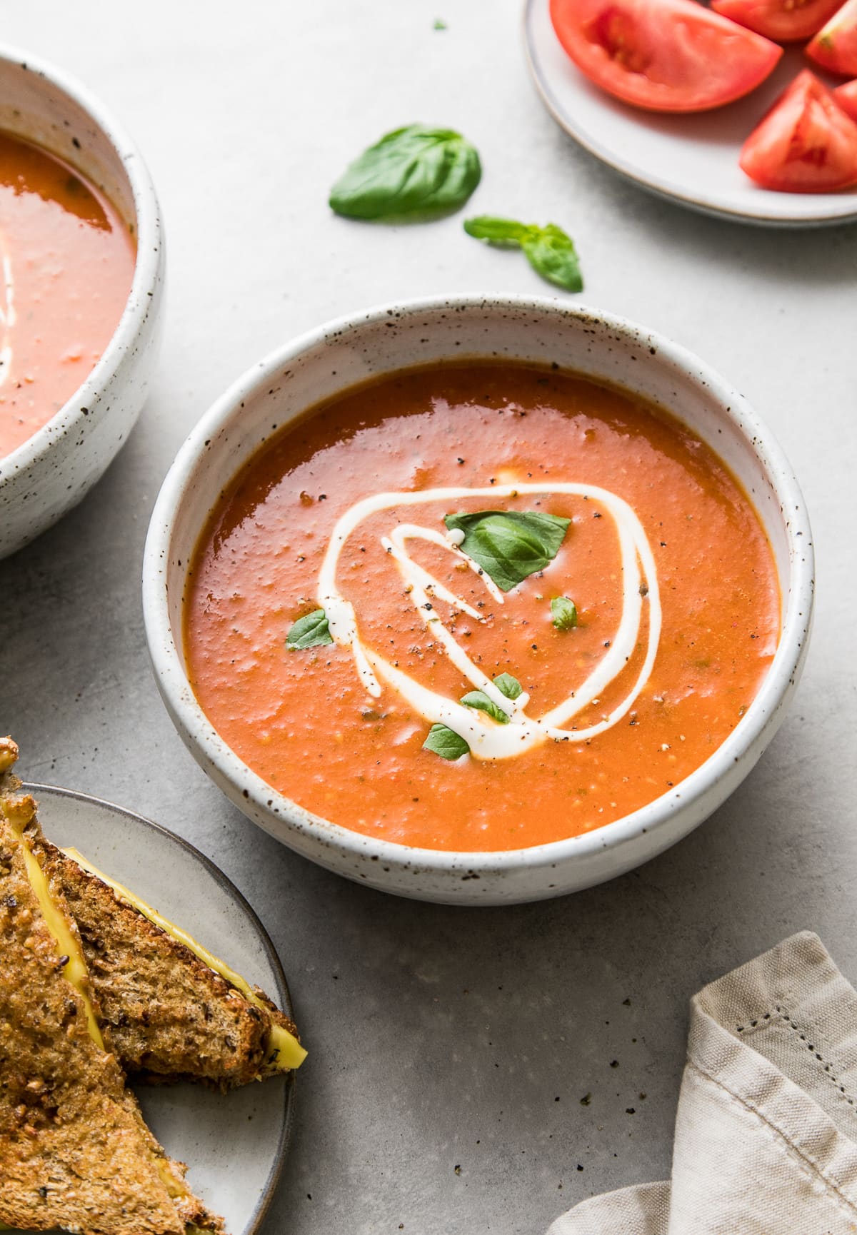 side angle view of bowl with serving of tomato basil soup and items surrounding.