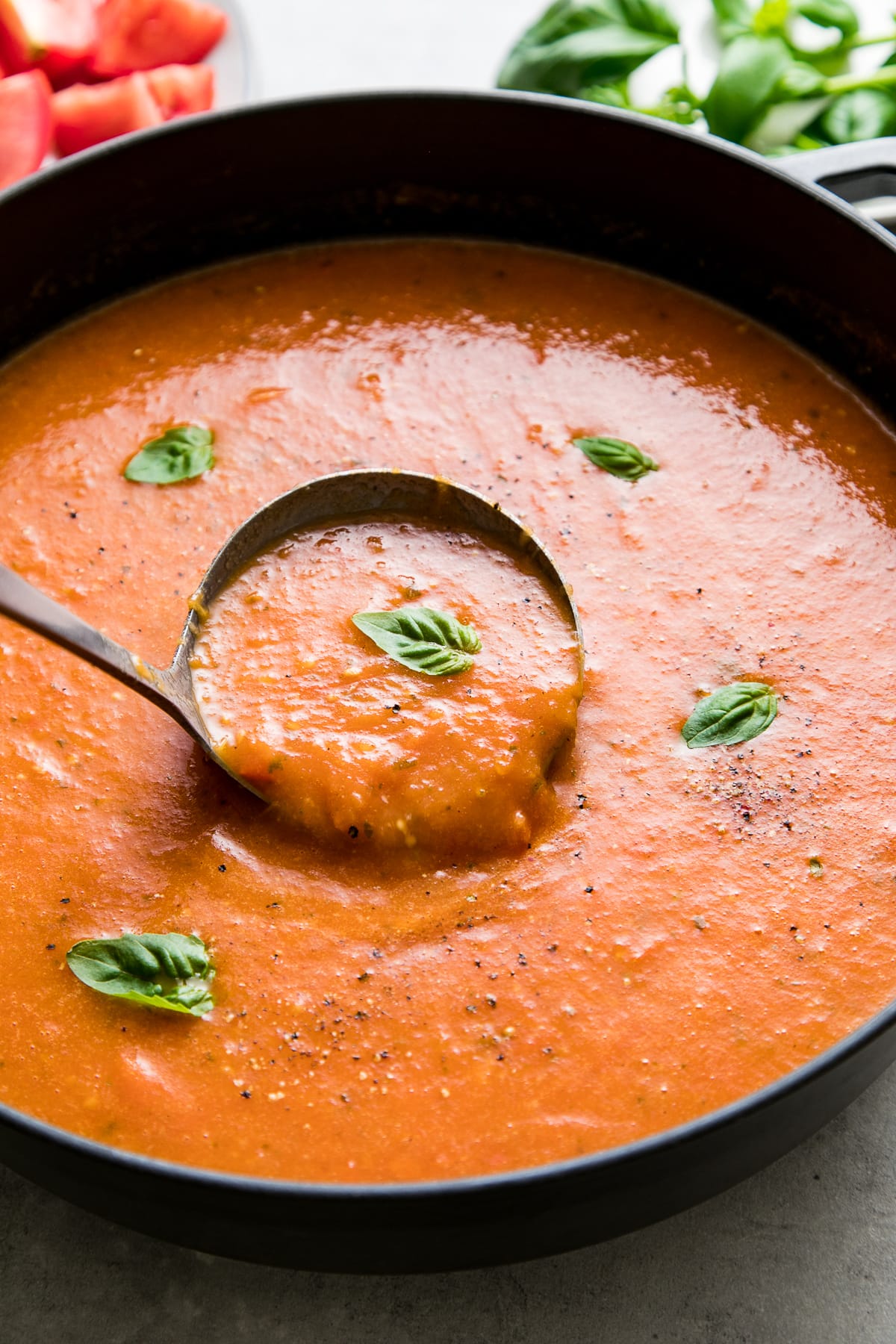 side angle view of a ladle full of easy tomato basil soup in a pot.