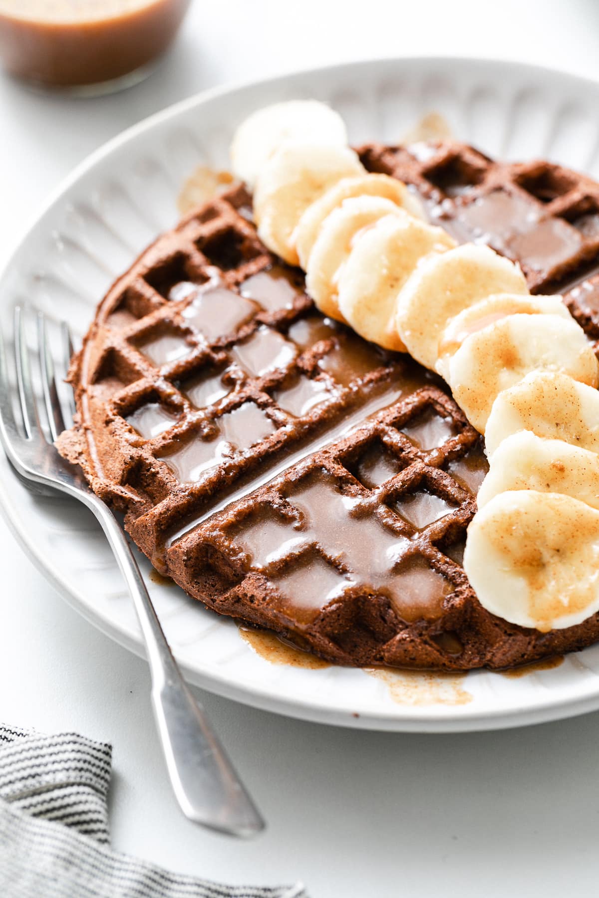 side angle view of chocolate vegan buckwheat waffles with banana and syrup.