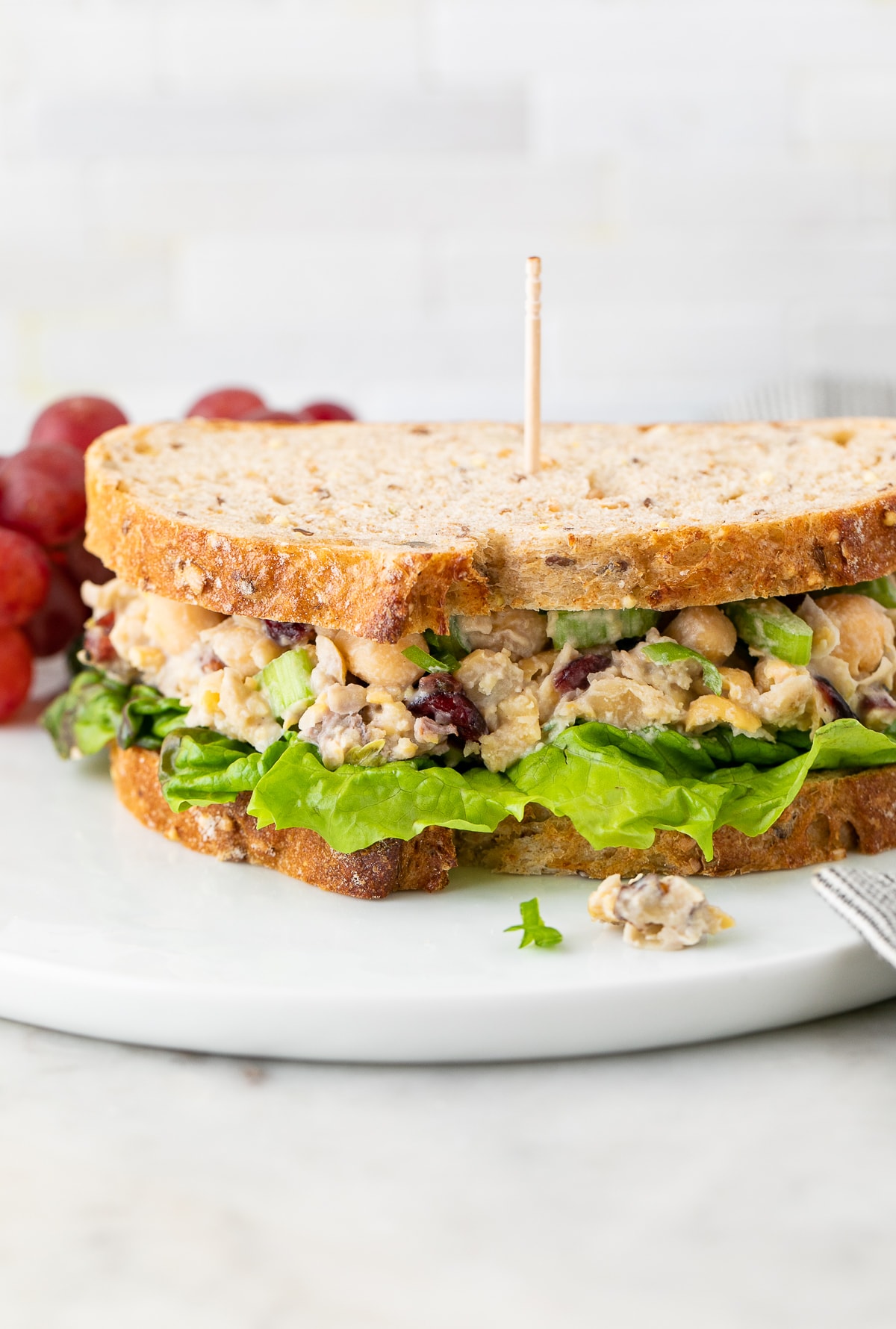 head on view of healthy vegan chicken salad sandwich on a plate with items surrounding.